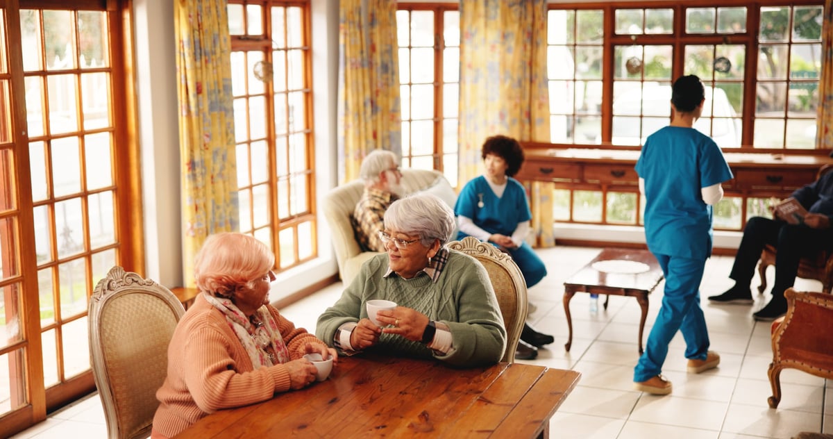 Two older women sharing coffee and conversation in a warm, comfortable home setting